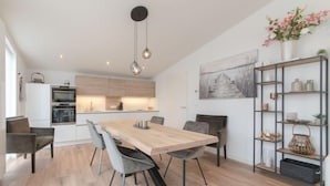 A modern kitchen with built-in appliances, a dining area with a wooden table and chairs, and a decorative shelf with various items.