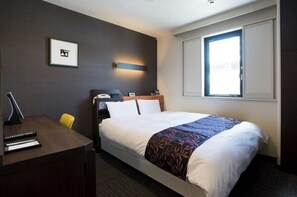 Comfortable room with a neatly made bed, bedside table, and desk with chair.