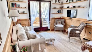 Una sala de estar acogedora con un sofá, dos sillones de mimbre, una mesa de centro de madera y un televisor sobre un mueble de madera.