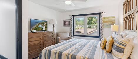 A bedroom with a bed, a ceiling fan, a window with curtains, a dresser, a chair, and a television.