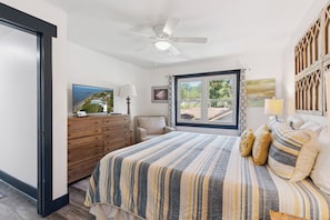 A bedroom with a bed, a ceiling fan, a window with curtains, a dresser, a chair, and a television.
