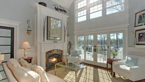A spacious living room with a fireplace, large windows, and a balcony. - Waterfront Villa near Hamptons with pool, hot tub & boat dock (Center Moriches)