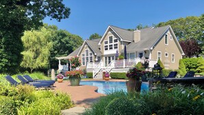 A two-story house with a swimming pool, sun loungers, and a garden with flowers. - Waterfront Villa near Hamptons with pool, hot tub & boat dock (Center Moriches)