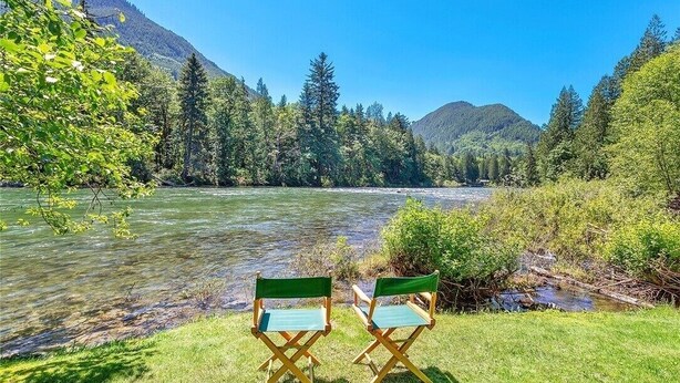 Two chairs facing a river with a forested mountain backdrop.