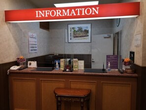 Un comptoir d’accueil avec une pancarte indiquant « RENSEIGNEMENTS », un tableau encadré accroché au mur et une porte portant un numéro.
