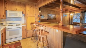 Interior de una cabaña de madera con cocina, barra y zona de estar.