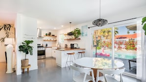 A modern kitchen with white cabinets, a central island, and a dining area with a glass table and white chairs.