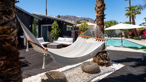 A hammock on a wooden deck with a pool and mountains in the background.