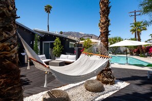 Un hamac sur une terrasse en bois, avec une piscine et des montagnes en arrière-plan.