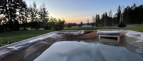 A hot tub in a backyard with a view of trees and a house in the background.