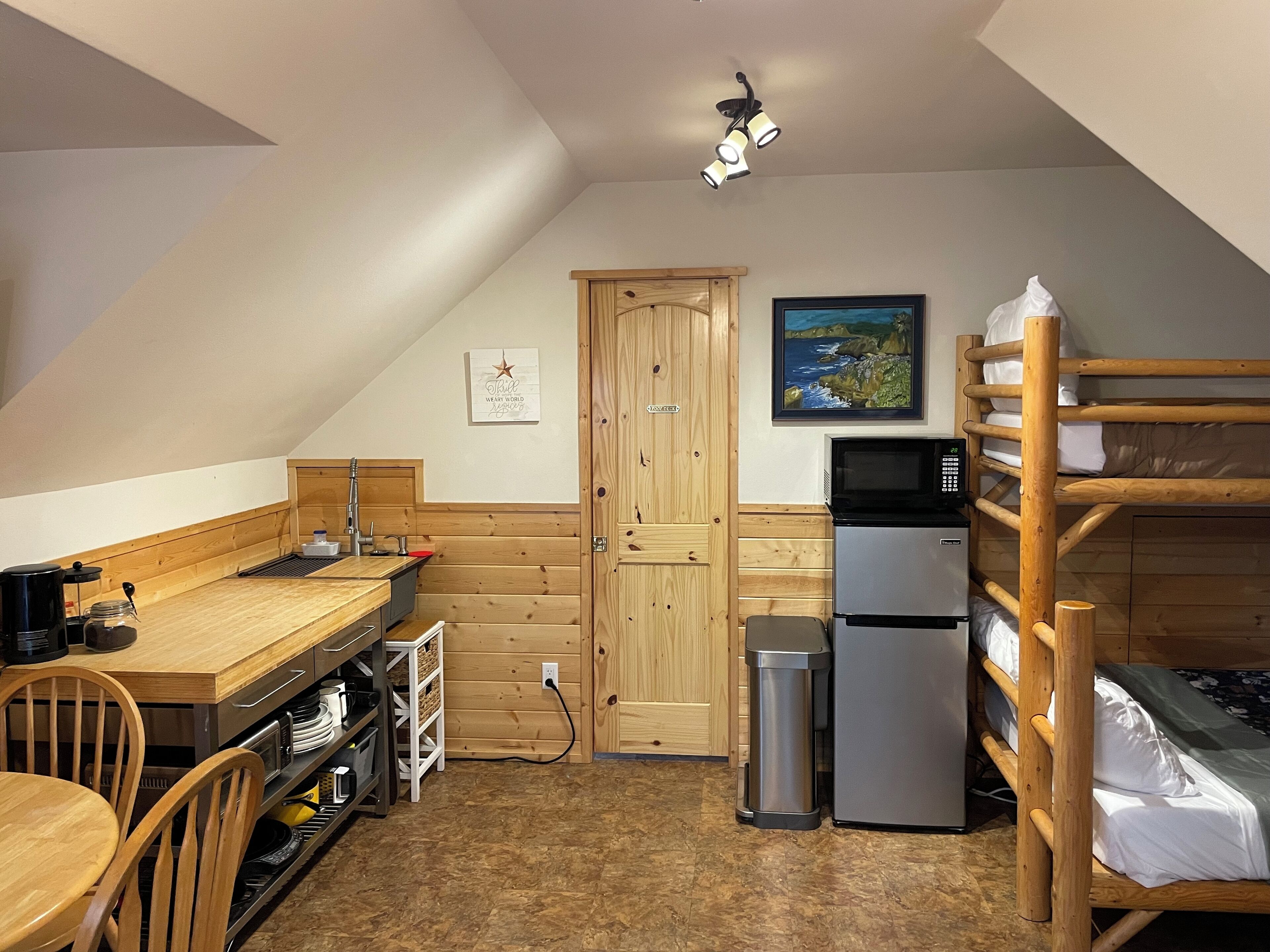 A compact kitchen with wooden cabinetry, a dining table, and a bunk bed.