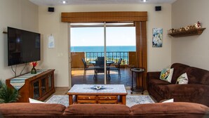 Ein Wohnzimmer mit Fernseher, einer Couch, einem Tisch und Meerblick durch eine Schiebetür.