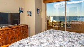 Ein Hotelzimmer mit Bett, Fernseher, Kommode und einem Balkon mit Blick auf die Stadt.