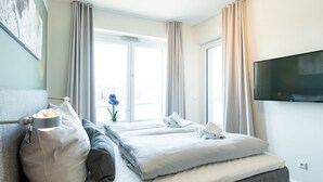 Een hotelkamer met een bed, een televisie, een raam met gordijnen en een plant.