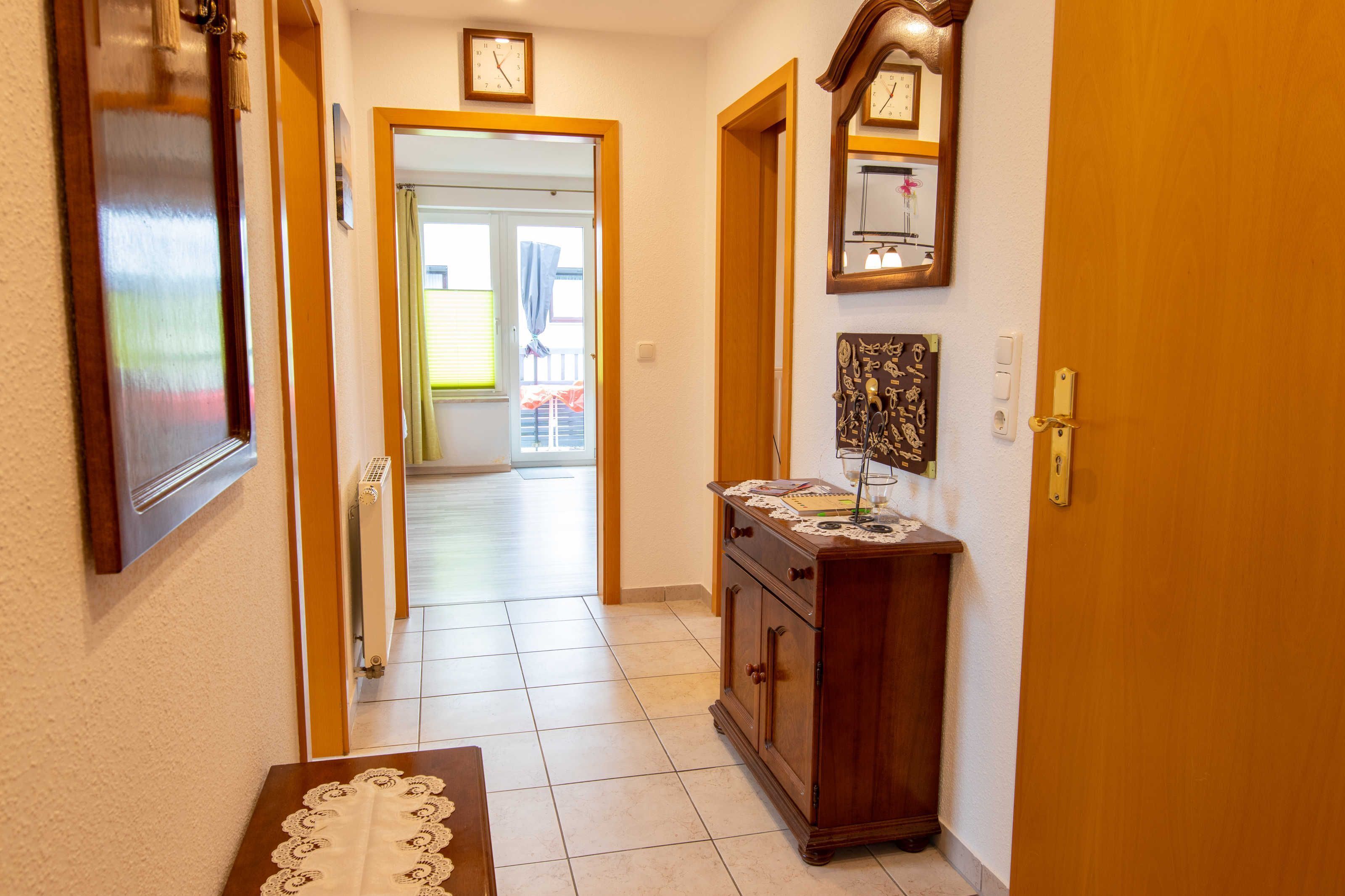 Ein Flur mit Holztür, Heizkörper, Tisch mit weißer Spitze und einem Schrank mit Dekoration.