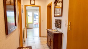 Un pasillo con puerta de madera, un radiador, una mesa con mantel de encaje y un aparador con adornos.