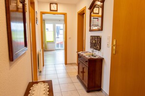 A hallway with a wooden door, a radiator, a table with a lace tablecloth, and a cabinet with decorative items. - Ferienwohnung Sukow - Ferienwohnung (Kröslin)