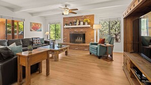 A living room with a fireplace, a ceiling fan, a TV, and a sofa.