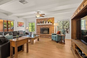 A living room with a fireplace, a ceiling fan, a TV, and a sofa.