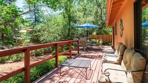 A wooden deck with a metal table and chairs, a red railing, and a view of trees and greenery.