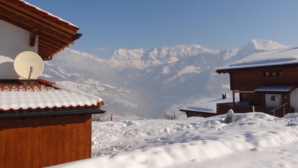 A wooden chalet with a satellite dish, surrounded by snow-covered mountains.