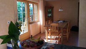 A dining area with a wooden table and chairs, a vase with flowers, and a bowl of fruit on the counter.