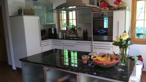 A modern kitchen with white cabinets, a granite countertop, and a large island. There are various kitchen appliances, including a coffee maker and a microwave. A window provides natural light, and a vase with flowers is on the island.