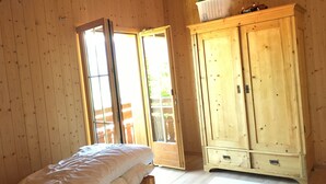 A wooden-paneled room with a bed, a wardrobe, and a sliding glass door leading to an outdoor area.