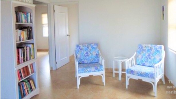 A room with a bookshelf, two patterned chairs, a small table, and a door.