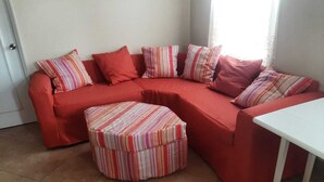 A red sectional sofa with striped pillows and a matching ottoman in a room with tiled flooring.