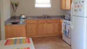 A compact kitchen with wooden cabinets, a white refrigerator, a stove, and a window providing natural light.