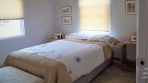 A bedroom with a bed, two bedside tables, a window, and a door.