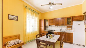 Une cuisine avec des meubles de rangement en bois, une table à manger avec des chaises, un banc et un ventilateur de plafond.