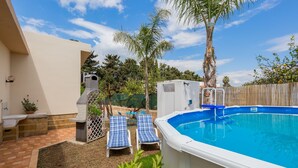 Un jardin avec une piscine, deux chaises longues, un espace barbecue et une clôture en bois.