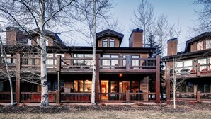 A two-story log cabin with a balcony, surrounded by trees and a wooden deck.