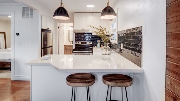 A modern kitchen with white cabinetry, a black backsplash, and a central island with stools.
