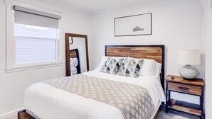A bedroom with a wooden bed frame, a bedside table with a lamp, and a window with blinds.