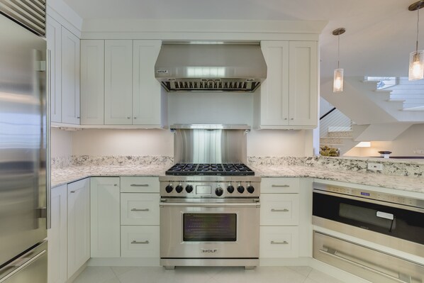 Una cocina moderna con electrodomésticos de acero inoxidable, armarios blancos y encimera de mármol.