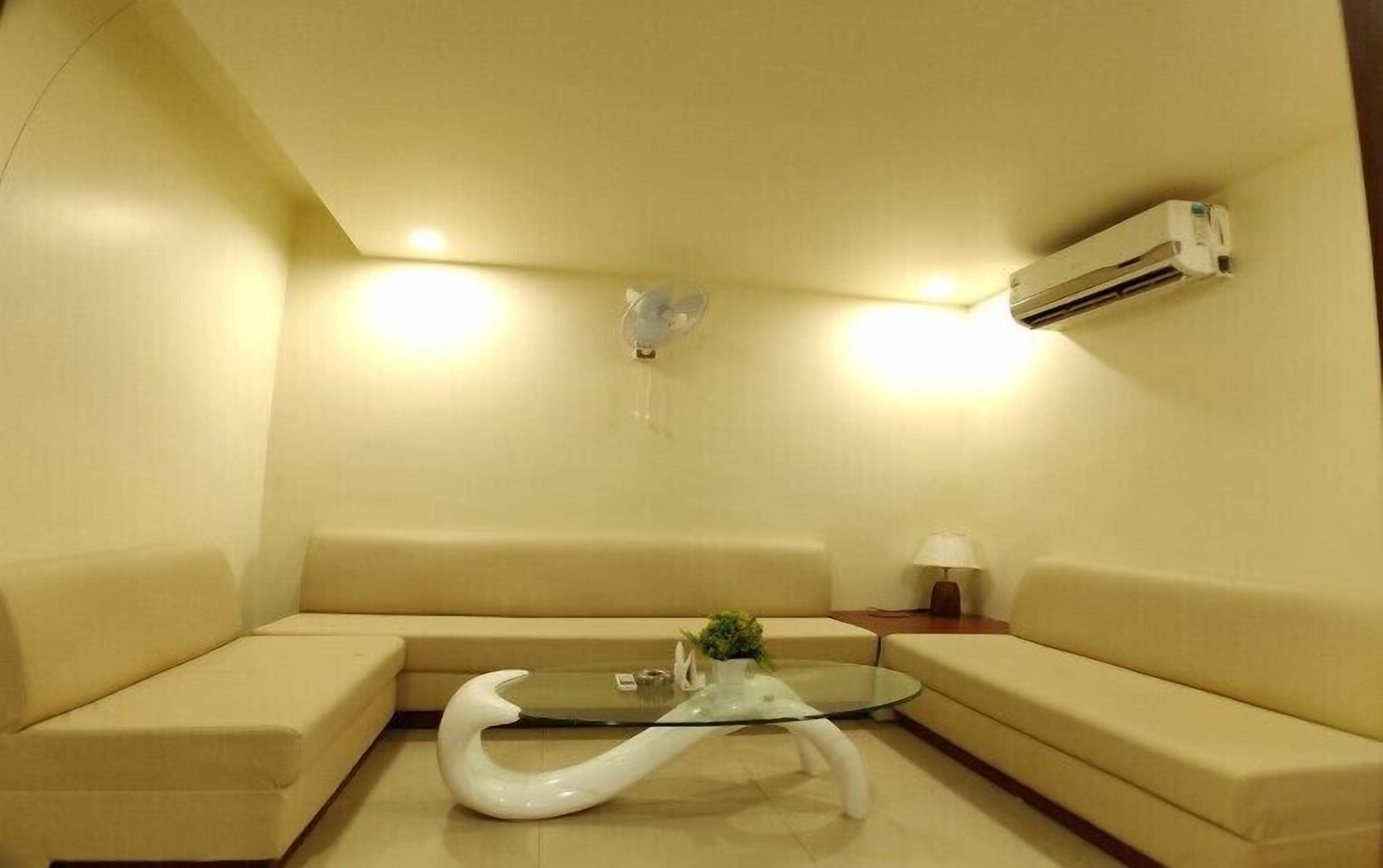 A living room with a glass coffee table, beige sofas, a lamp, and an air conditioning unit on the wall.