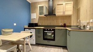 A compact kitchen with wooden cabinets, a built-in oven, and a microwave. - STUDIO LILOU (Lons-le-Saunier)