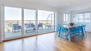 En rummelig stue med en stor skydedør, der fører til en terrasse, et spisebord med blå stole og udsigt over landskabet.