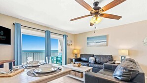 Un soggiorno moderno con zona pranzo, ventilatore a soffitto, vista sull'oceano e cartello che indica un affitto per vacanze.