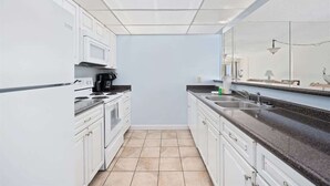 A modern kitchen with white cabinets, a black countertop, and a tiled floor. - Moondriter 606 - Beach Front Condo (Panama City Beach)