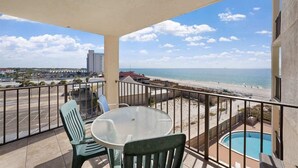 A balcony with a glass table and chairs, a pool, and a view of the beach and ocean. - Moondriter 606 - Beach Front Condo (Panama City Beach)