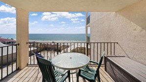 A balcony with a glass table and chairs, overlooking a beach and ocean. - Moondriter 606 - Beach Front Condo (Panama City Beach)