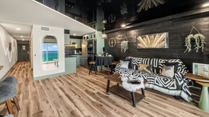 Un intérieur moderne avec un canapé à motifs noir et blanc, un plancher en bois et un coin cuisine visible à travers une arche.