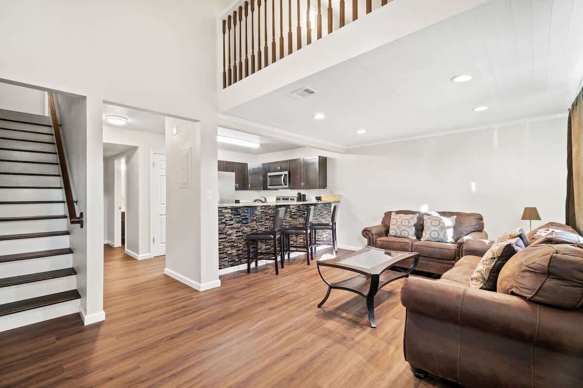 A spacious living area with a staircase, a kitchen with a stone backsplash, and a dining area with bar stools.