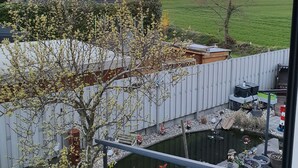 A view of a backyard with a wooden fence, a small pond, and various potted plants. - Schöne Ferienwohnung in Ruhiger Wohnsiedlung mit Unverbautem Feldblick (Wankendorf)