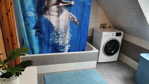 A bathroom with a shower curtain depicting a dolphin, a washing machine, and a potted plant. - Schöne Ferienwohnung in Ruhiger Wohnsiedlung mit Unverbautem Feldblick (Wankendorf)
