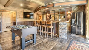 Eine gemütliche Bar mit einer Tischfußballplatte, einer Theke aus Stein und einem großen Kühlschrank.